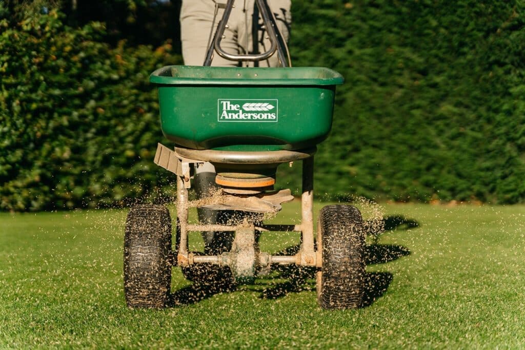 A seed spreader sowing new grass seed over a lawn