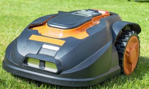 Black and orange robot lawnmower on a lawn. 