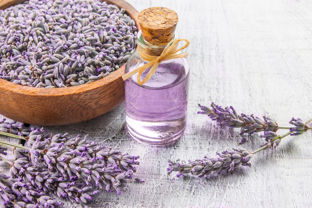 A bottle of lavender oil and sprigs of lavender in a wooden bowl